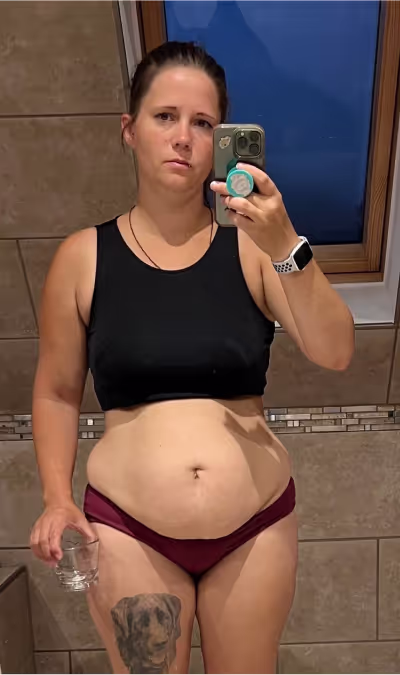 Eine Frau in Sport-BH und Unterwäsche macht ein Selfie im Spiegel und hält ein Glas.