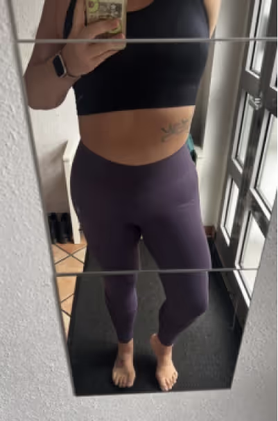 Eine Frau in Sport-BH und lila Leggings macht ein Selfie im Spiegel.
