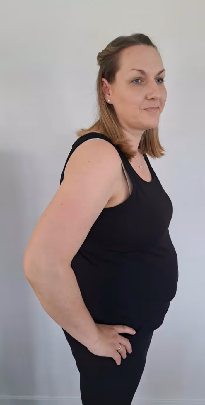 Eine Frau mit einem Dutt und seitlich hochgesteckten Haaren steht lächelnd vor einer weißen Wand.